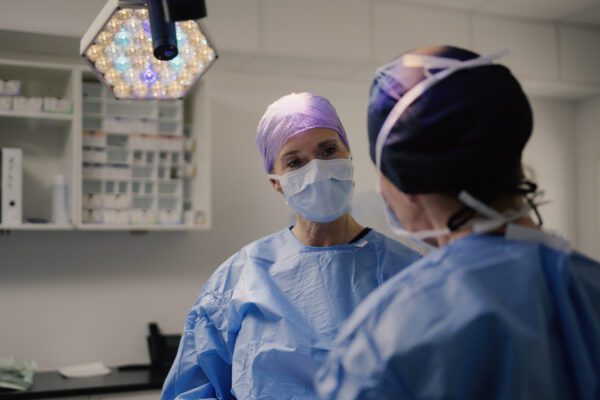 To kirurger i operationsstue med lilla operationshuer og blå kitler