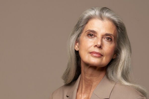 Kvinde med langt gråt hår i beige jakke på neutral baggrund