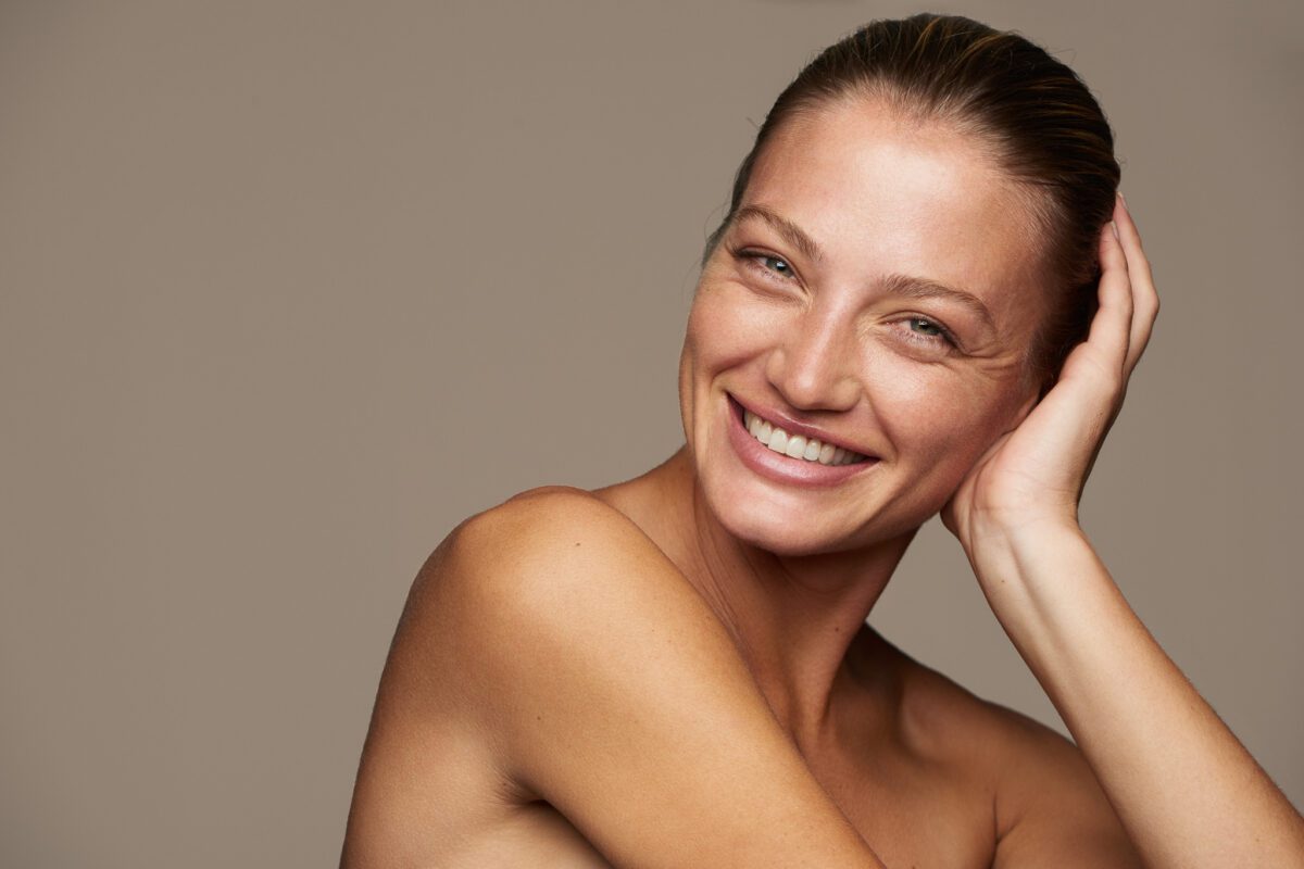 Smilende kvinde med hånden ved håret mod beige baggrund