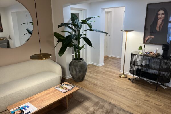Venteområde i klinik med beige sofa, stort spejl og grøn plante